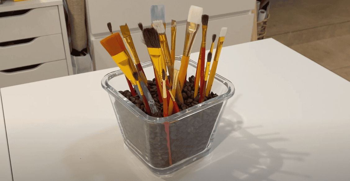 Paint brushes arranged in a clear container filled with coffee beans