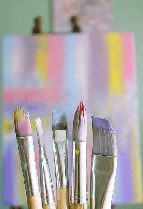 many paintbrushes, painted picture behind