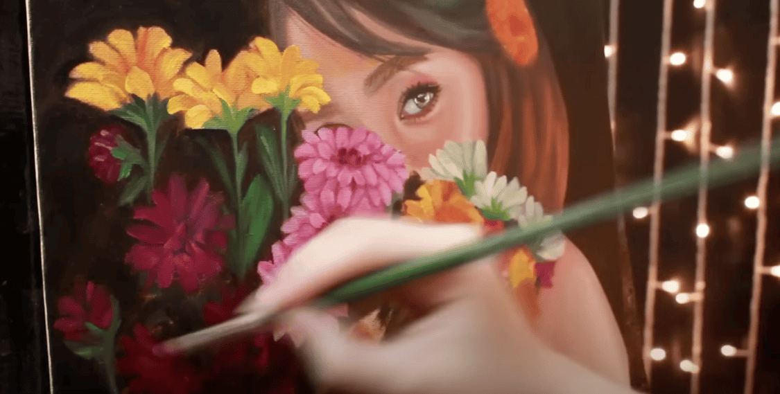 Photo of a blurred hand holding a brush, painting a girl surrounded by numerous flowers