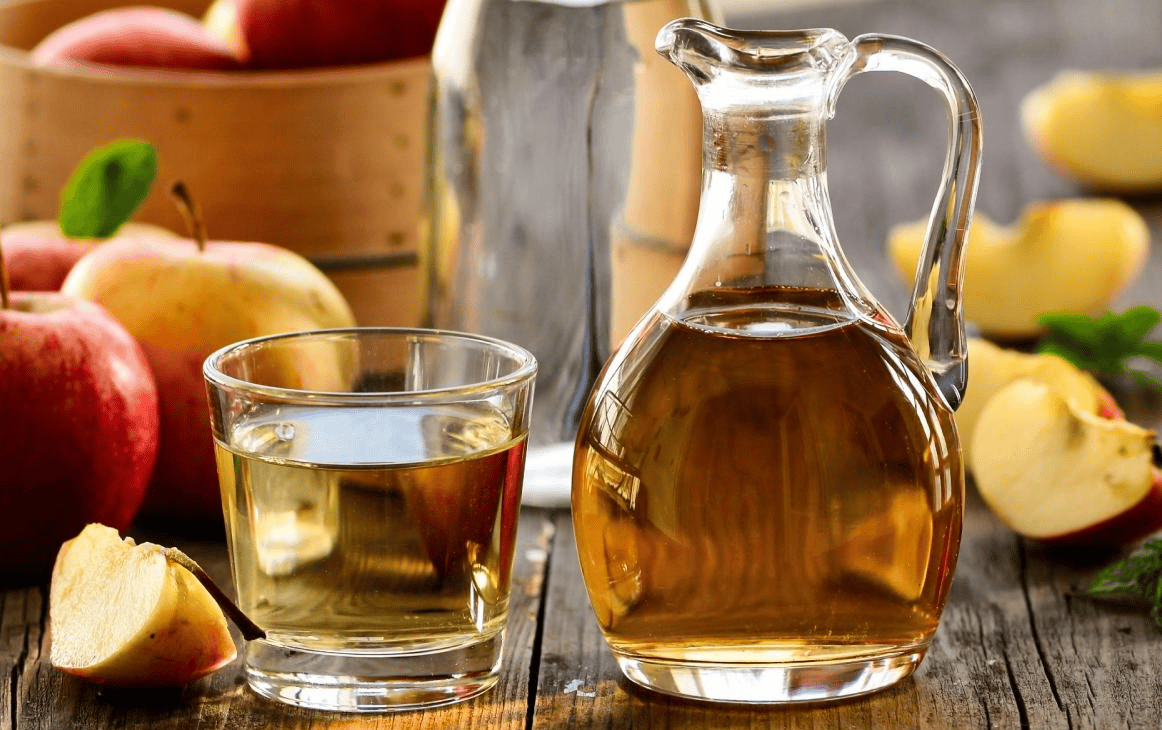 Vinegar in a glass, apples on the table