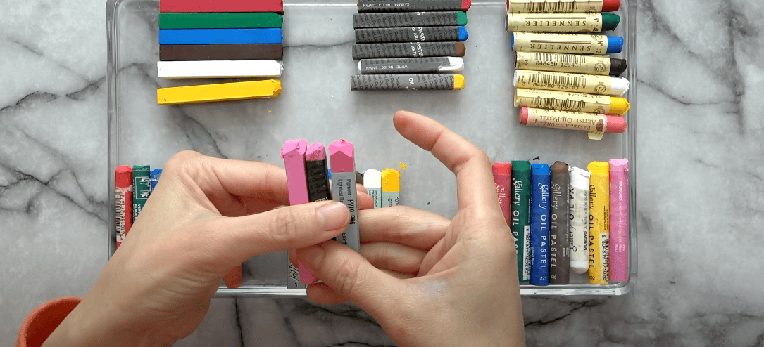 Photo of various oil pastels with three of them being held by a hand
