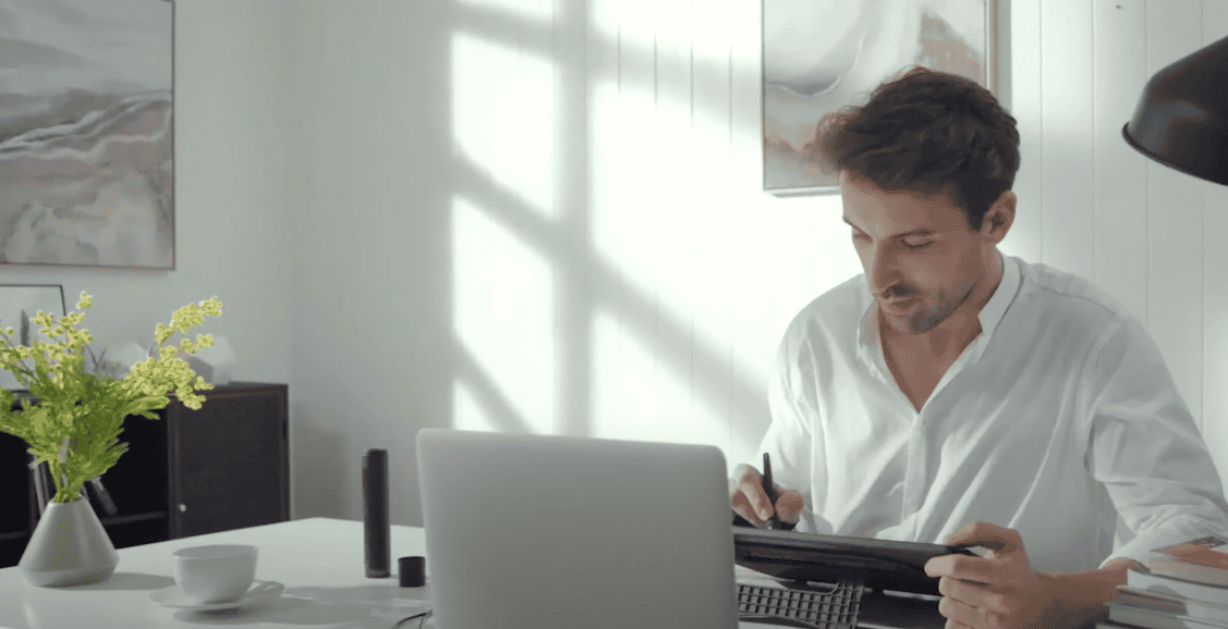 Photo of a guy sitting with a drawing pad and a laptop in front of him, actively working on the drawing pad