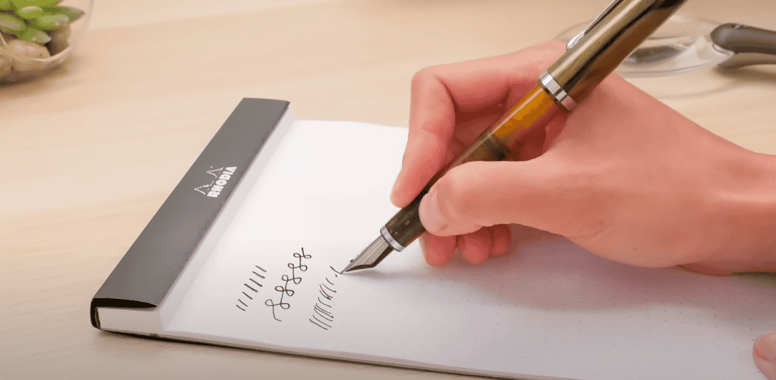 Photo of a hand writing in a writing pad using a fountain pen