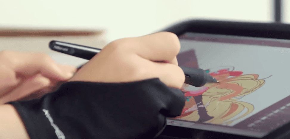 Photo of a hand wearing drawing gloves, holding a digital stylus and creating a drawing on a drawing pad